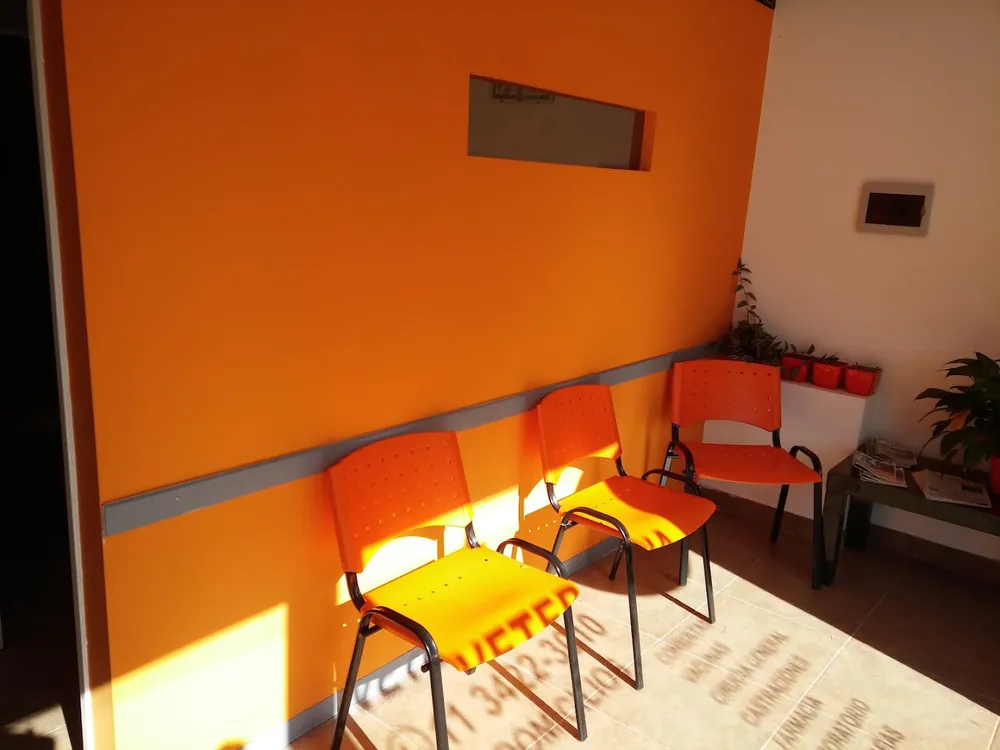 Sala de espera con pared naranja y tres sillas naranjas al sol